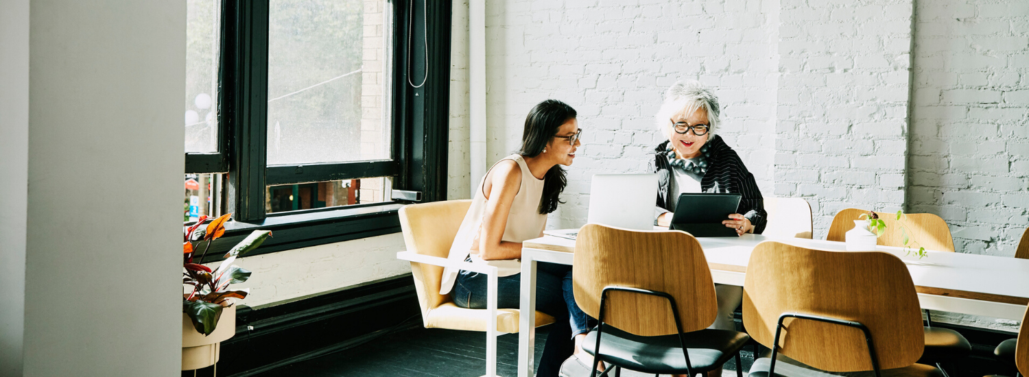 Two women sitting at a desk looking at a laptop